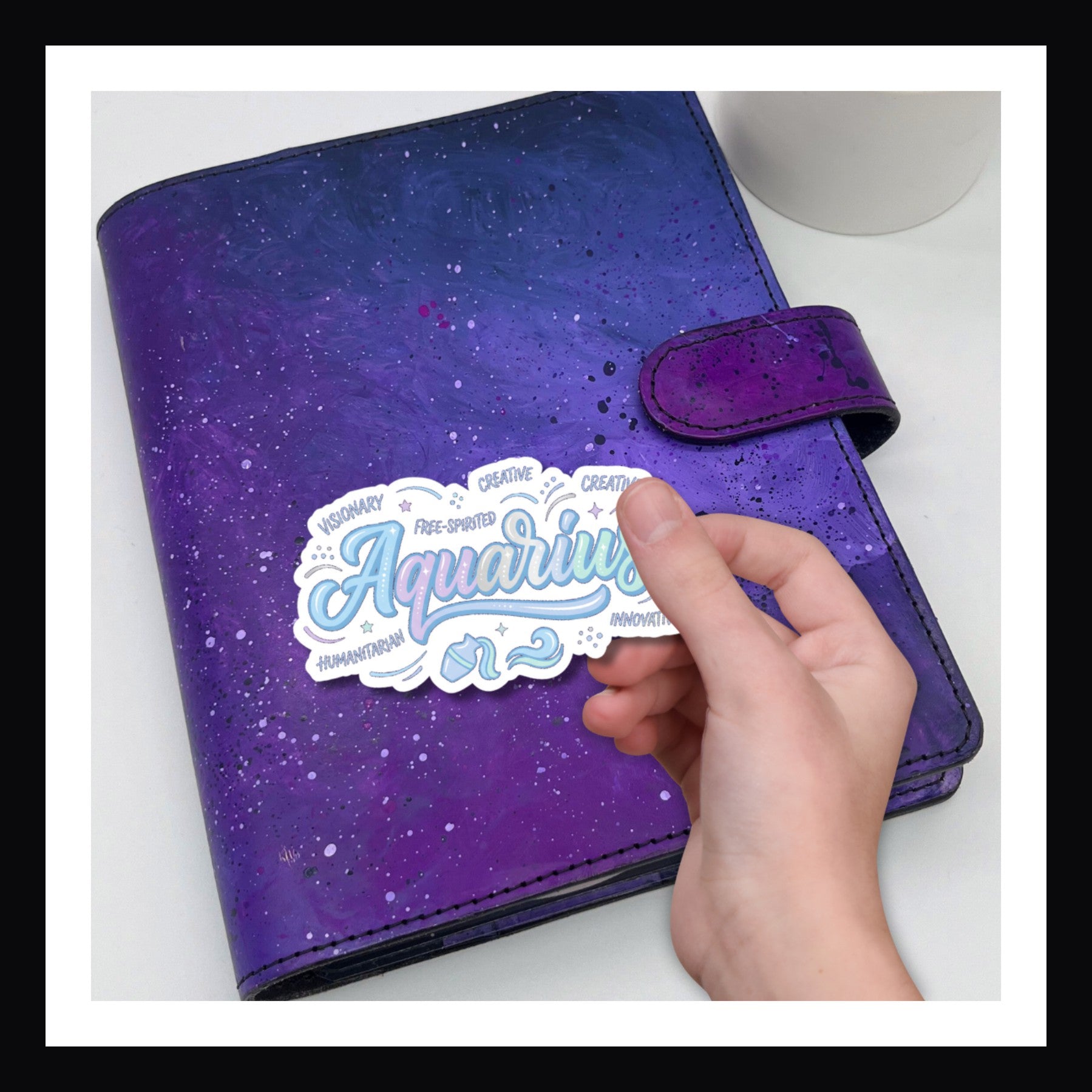Purple planner with a hand placing an 'Aquarius' sticker on it