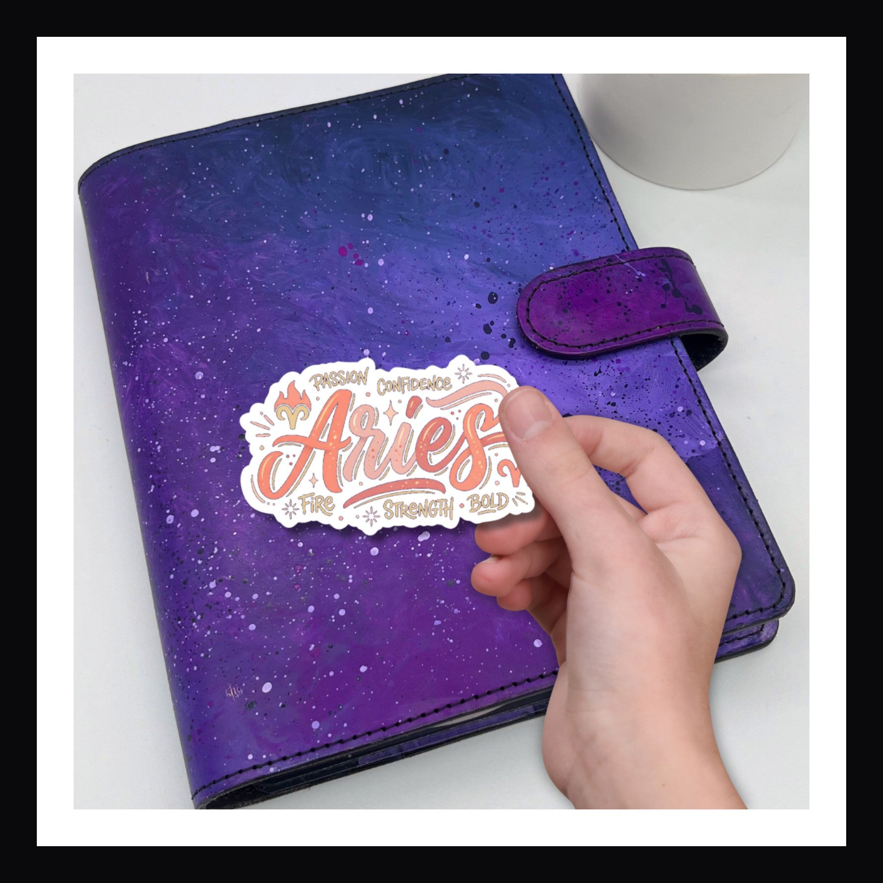 Purple planner with a 'Aries' sticker held by a hand on a white background