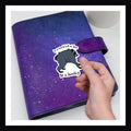 Be A Jimothy Die Cut Sticker - sticker featuring the quirky raccoon with the phrase "In a world full of Jims, be a Jimothy!"  Shown her over a purple planner.