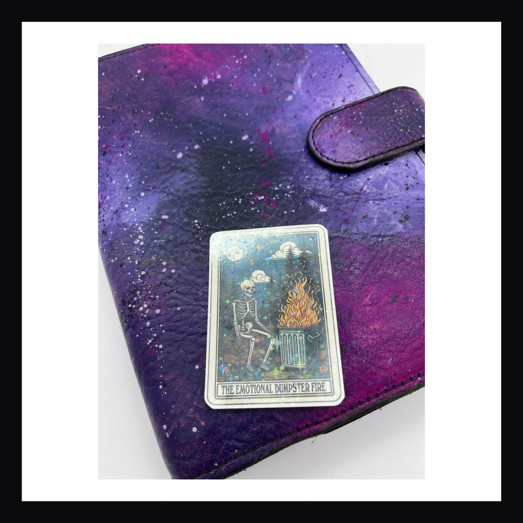 Alternative Tarot Die Cuts - Dumpster Fire is a holographic die cut sticker featuring a skeleton sitting in front of a garbage can on fire.