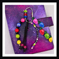 Festive AF Carabiner Bag Charm featuring a handmade charm of cascading Christmas light bulbs, a paracord knot with bead, additional bead detail and a friendship-bracelet-style beaded tag that reads "festive AF"