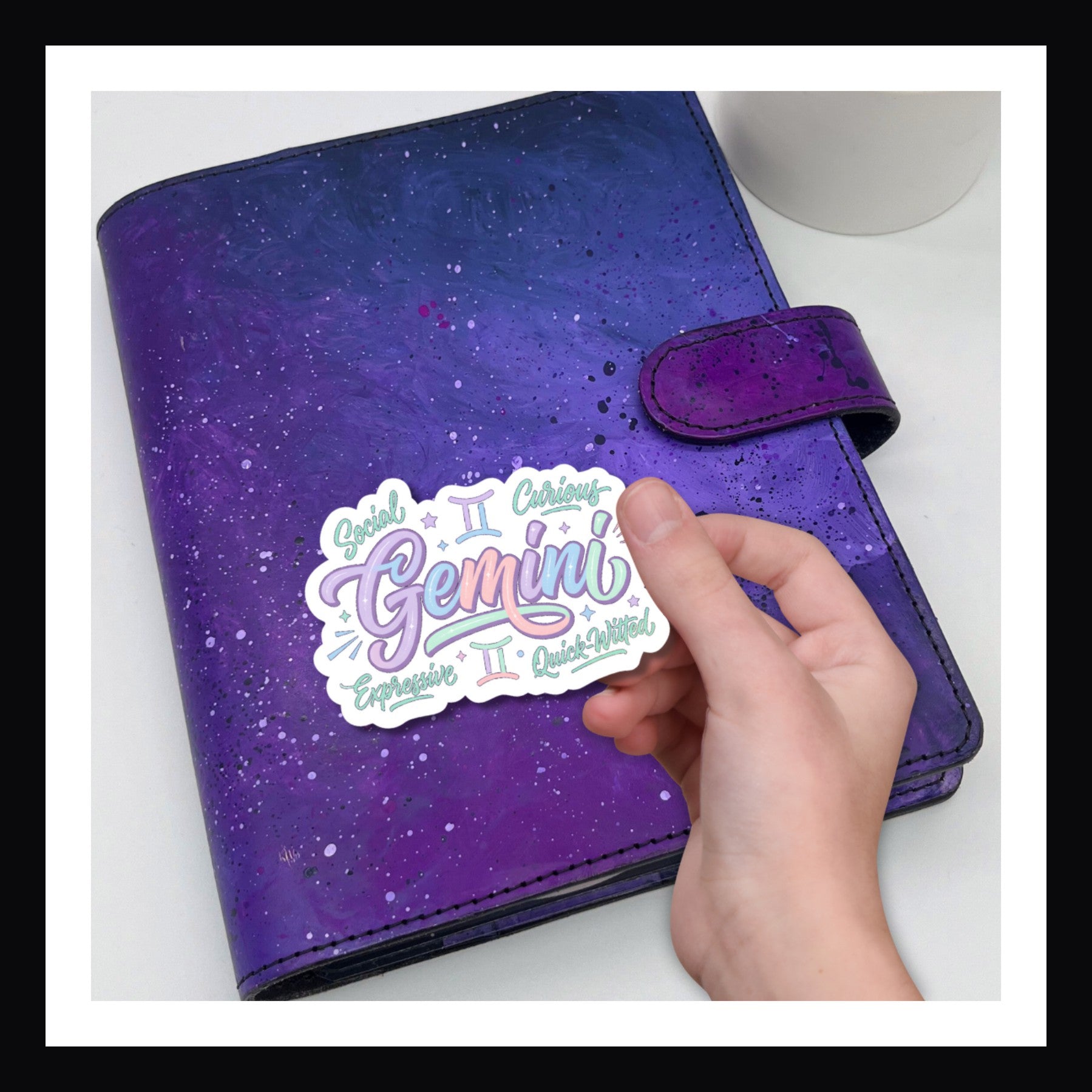 Purple planner with a 'Gemini' sticker held by a hand on a white background