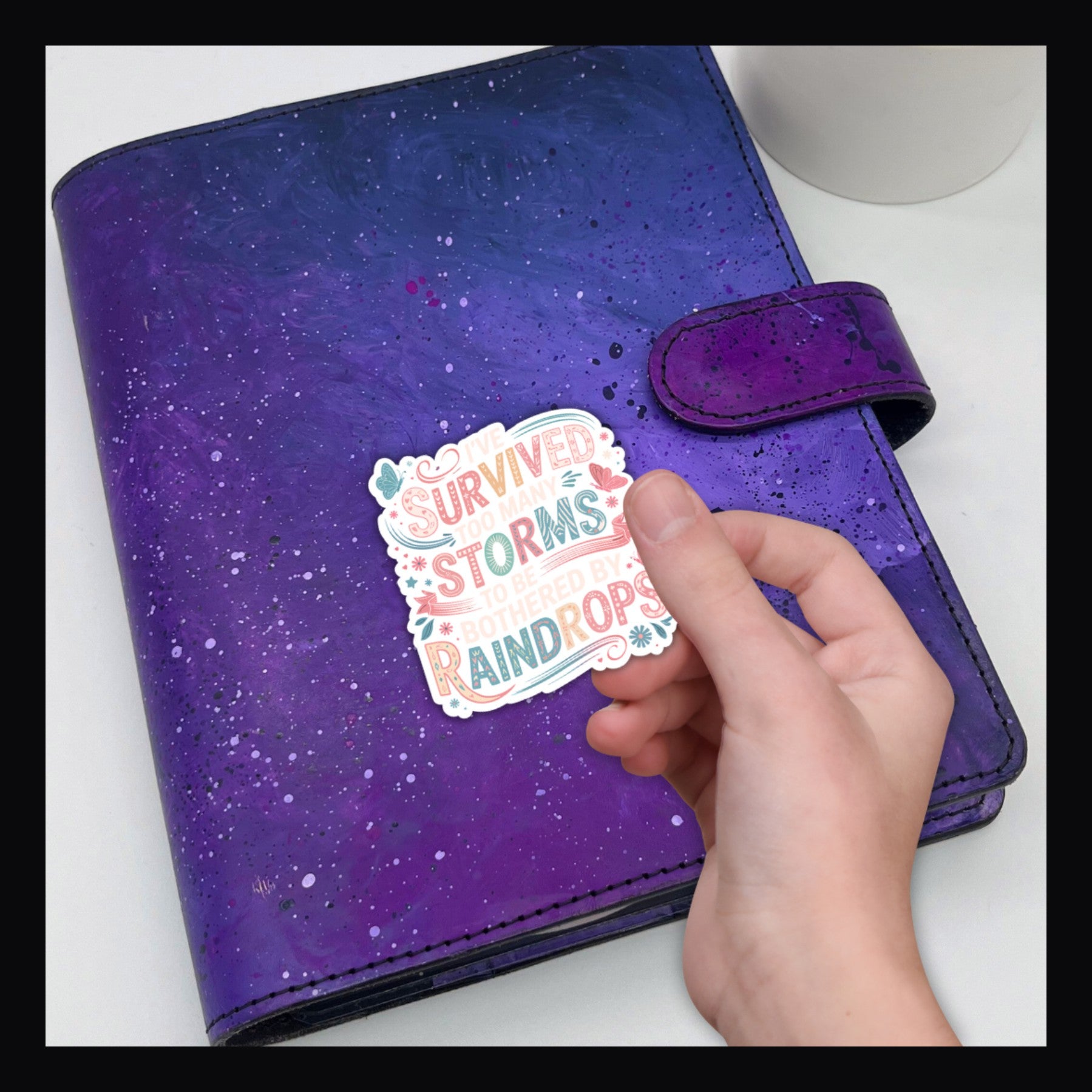 I've Survived Die Cut Sticker reads "I've survived too many storms to be bothered by raindrops".  Shown on a purple planner.