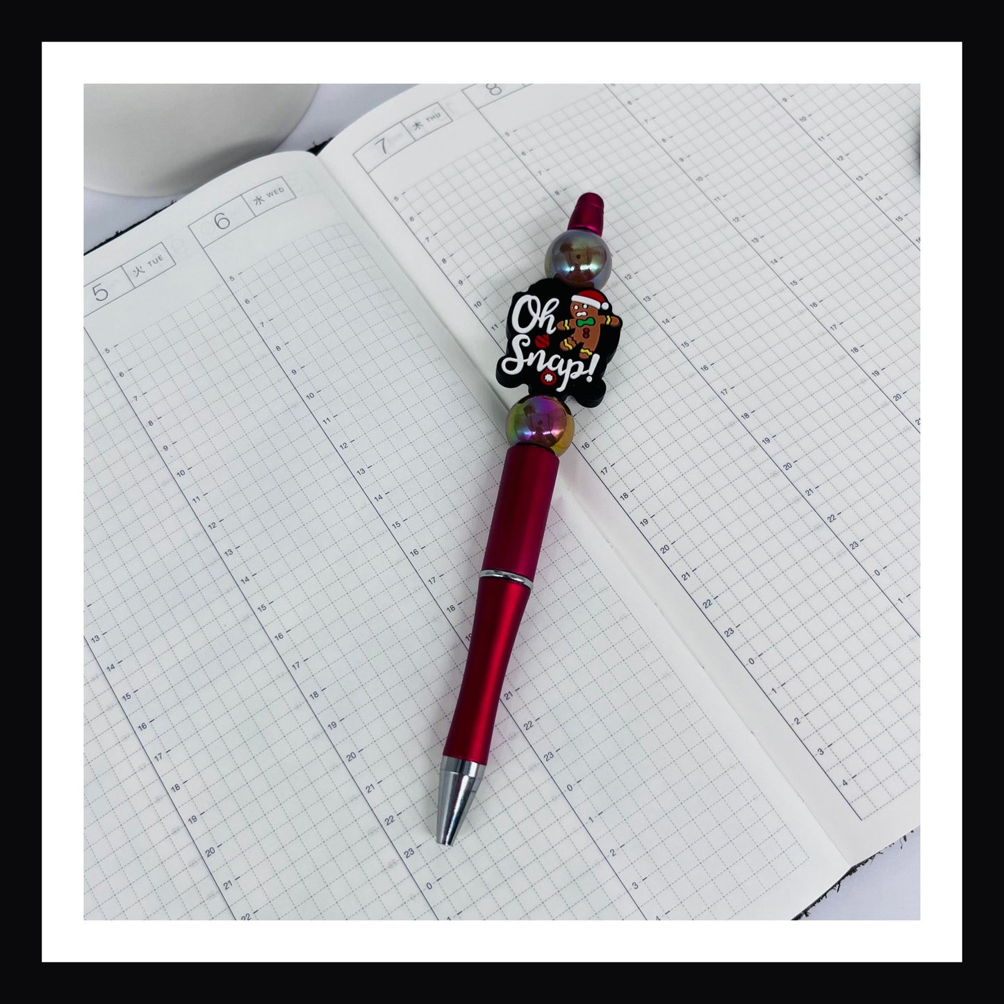 Oh Snap Pen is a black ink ballpoint pen.  It features a red barrel, two opalescent beads and one silicone bead featuring a gingerbread man and a "oh snap" message. 