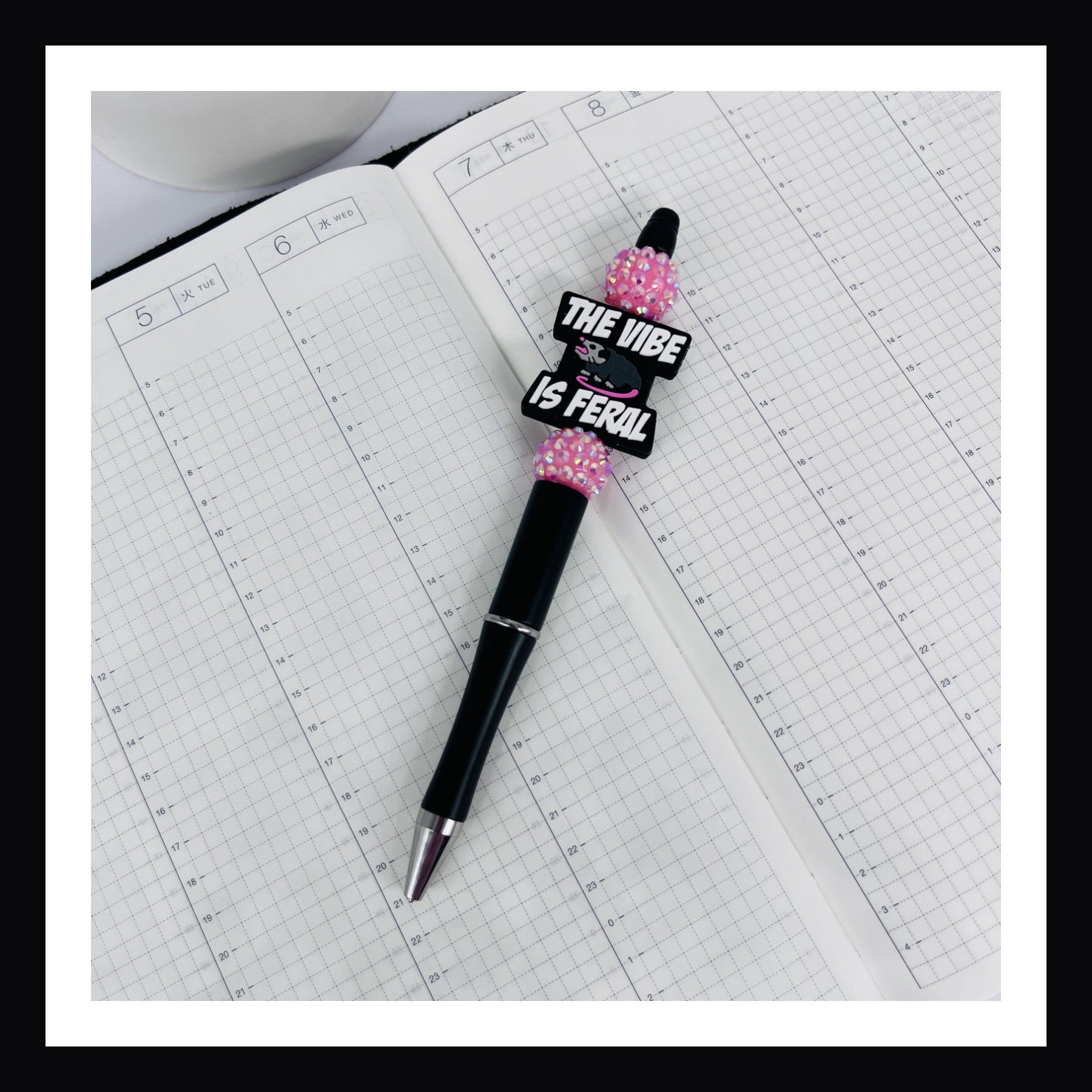 Feral Vibe Pen is a black ink ballpoint pen featuring a matte black barrel, two rhinestone beads and a silicone focal bead with an opossum and a message that reads "the vibe is feral"