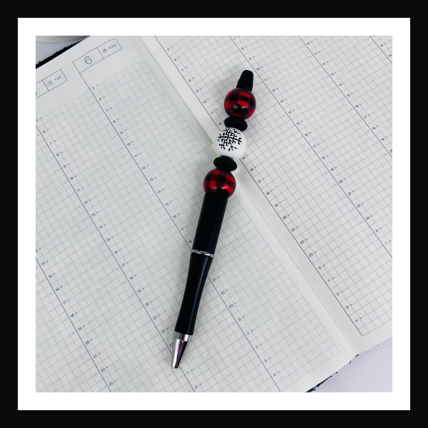 Snowflakes & Scarves Pen is a black ink ballpoint pen featuring 3 wood beads with two silicone spacers.  Two of the three beads feature red buffalo plaid, the third bead features a snowflake.