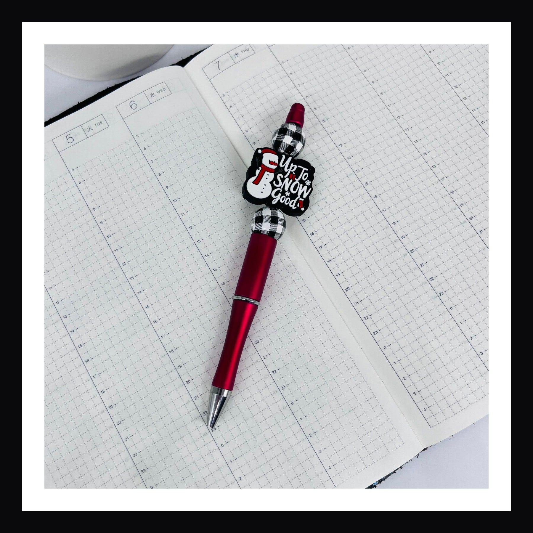 Snow Good Pen is a black ink ballpoint pen.  It features a metallic red barrel, two buffalo plaid wood beads and a silicone focal bead with a snowman and "Up to Snow Good" message. 