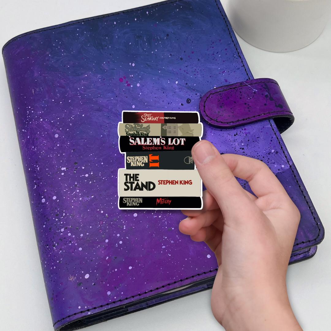 Purple planner with sticker featuring Stephen King book titles, held by a hand.
