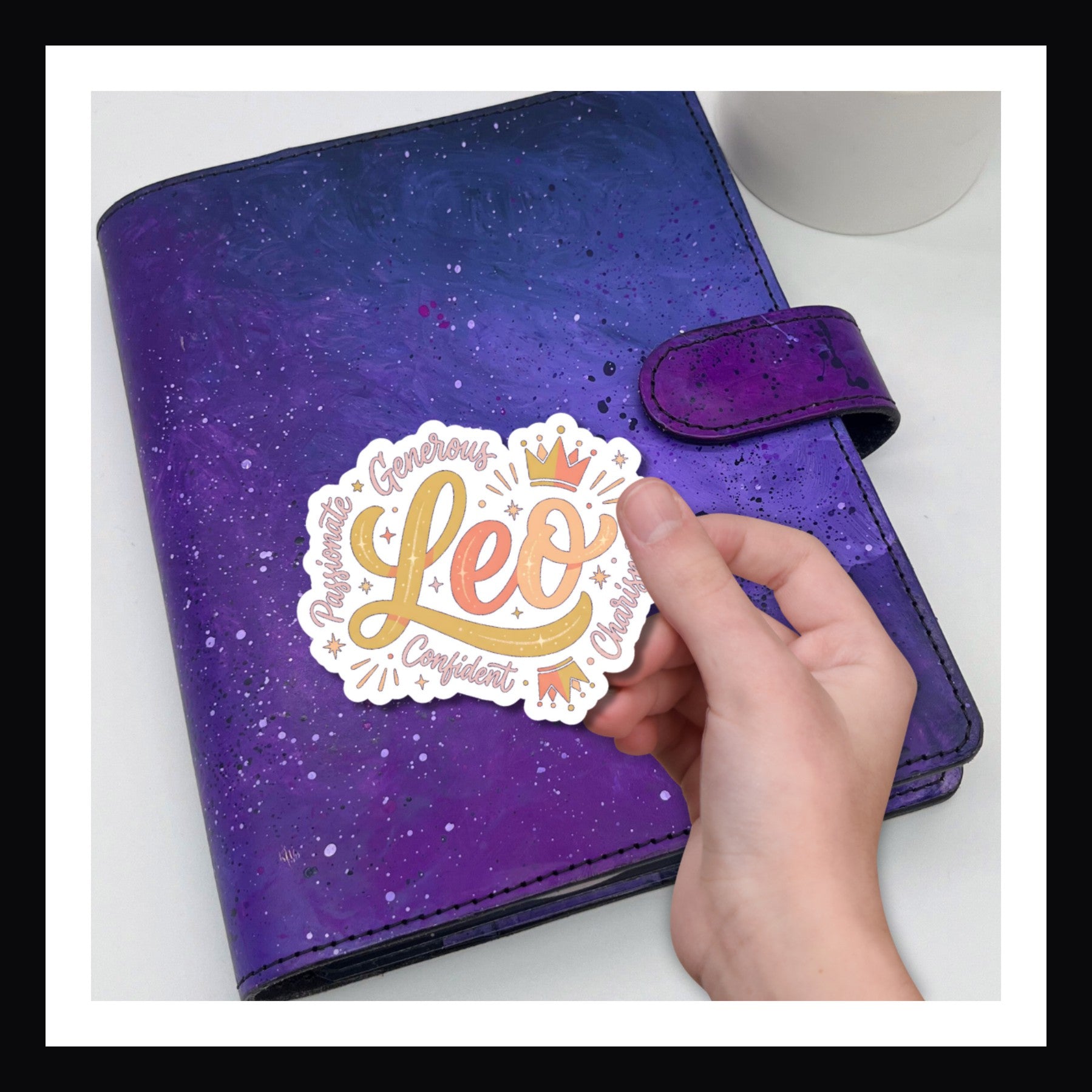 Purple planner with a hand holding a 'Leo' sticker against a white background