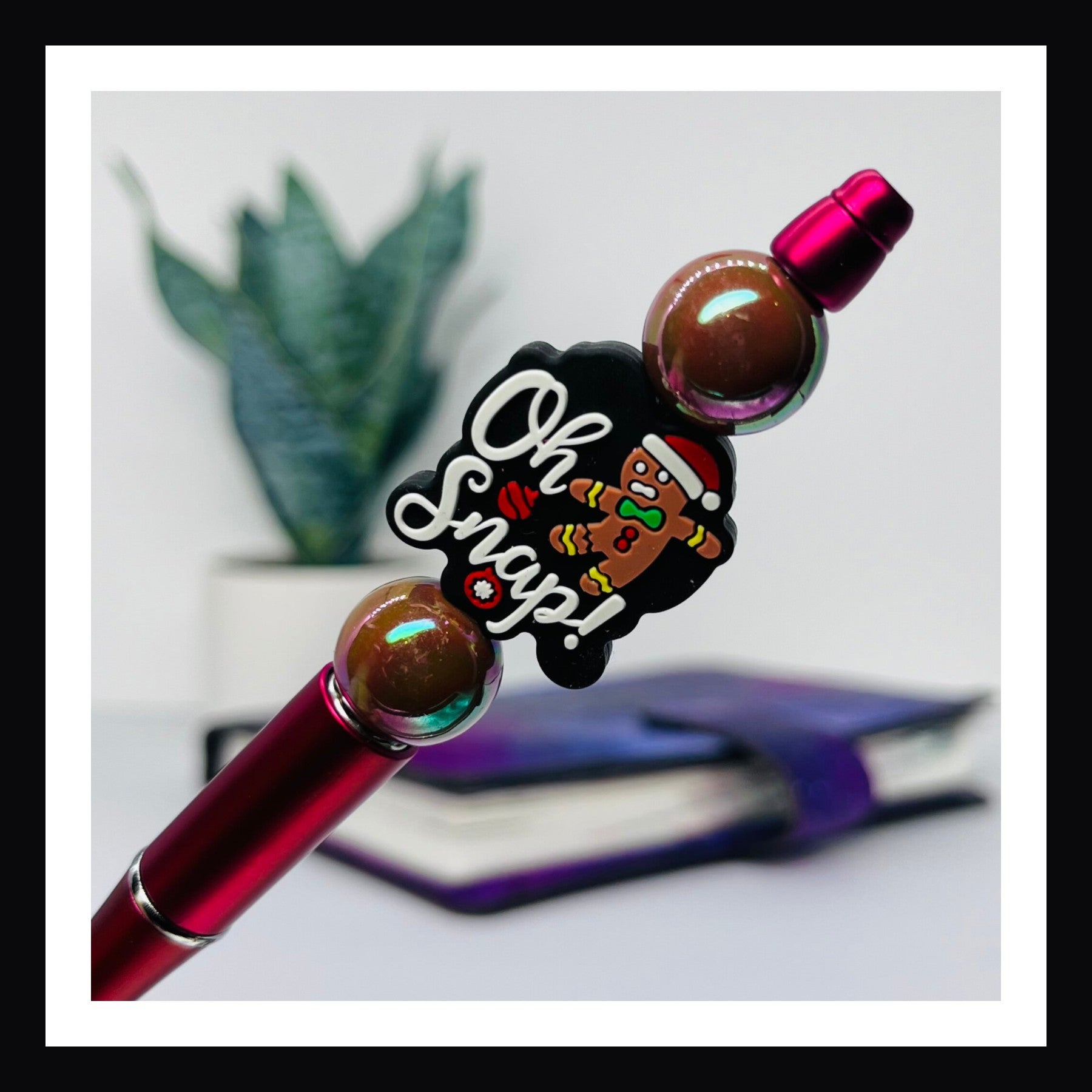 Oh Snap Pen is a black ink ballpoint pen.  It features a red barrel, two opalescent beads and one silicone bead featuring a gingerbread man and a "oh snap" message. 