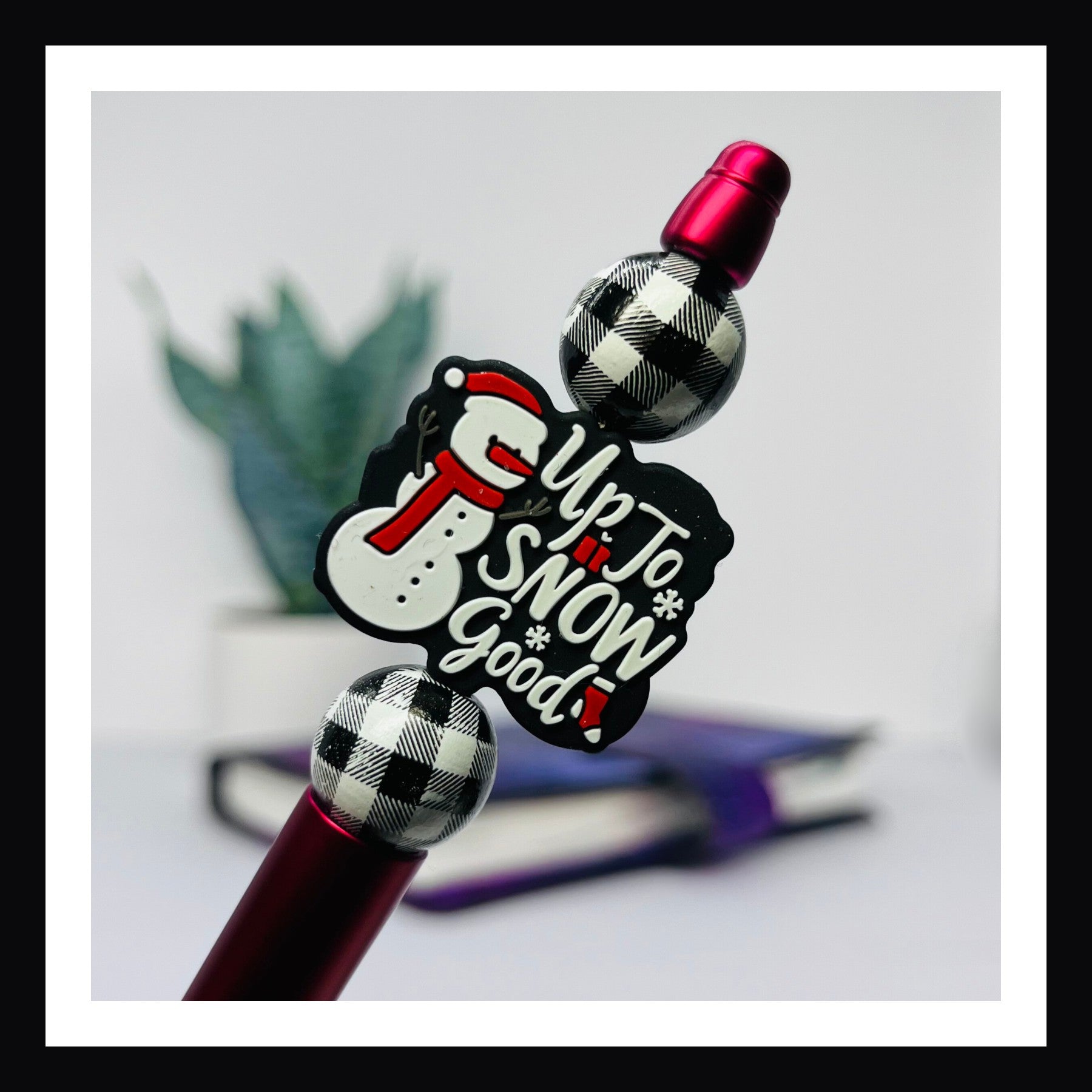 Snow Good Pen is a black ink ballpoint pen.  It features a metallic red barrel, two buffalo plaid wood beads and a silicone focal bead with a snowman and "Up to Snow Good" message. 