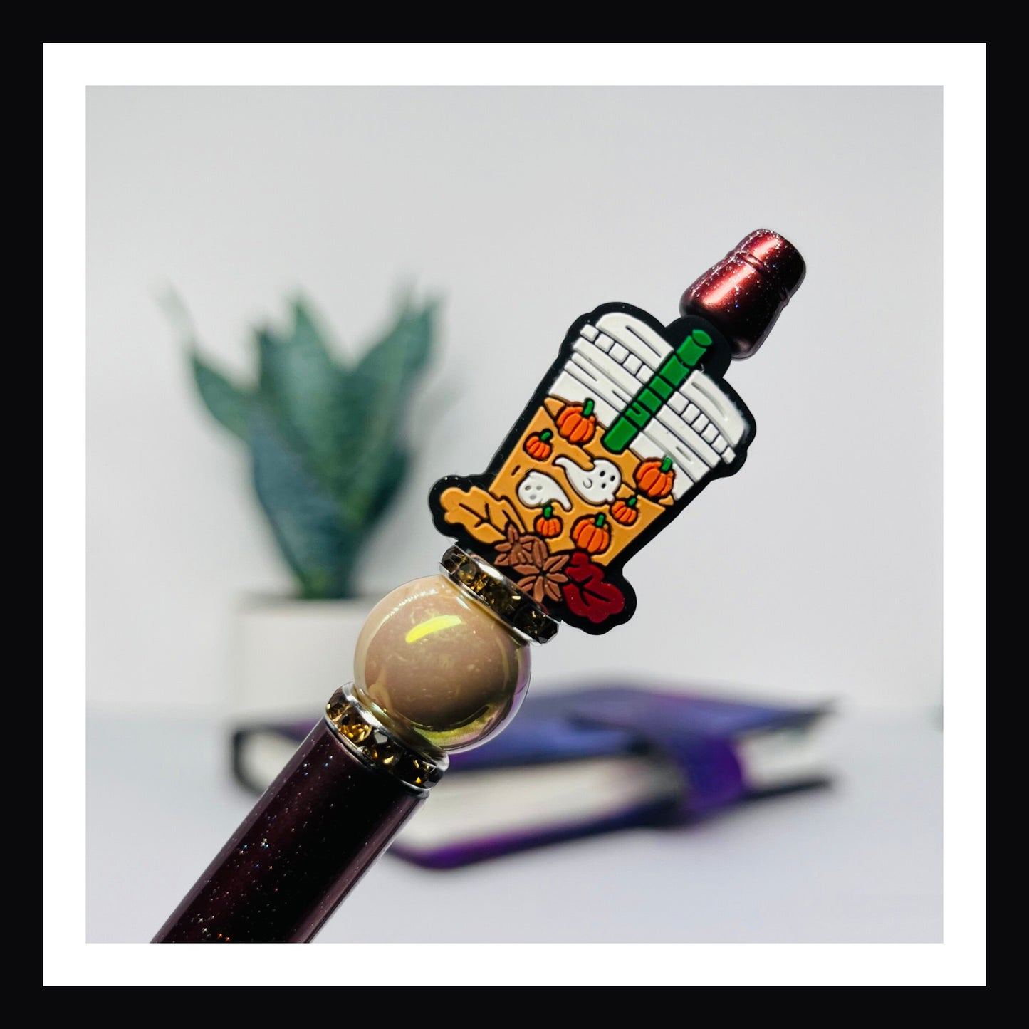 Pumpkin Spice Ghosts Pen is a black ink ballpoint pen.  It features a glittery brown barrel opalescent bead, rhinestone spacers and a silicon bead of a coffee drink with leaves, pumpkins and ghosts. 