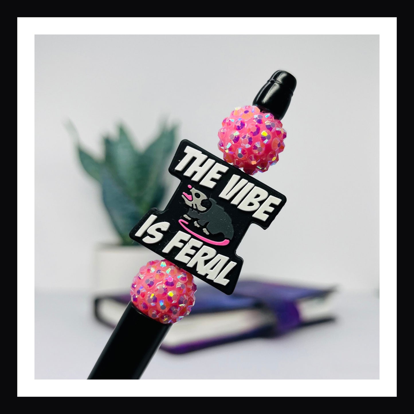 Feral Vibe Pen is a black ink ballpoint pen featuring a matte black barrel, two rhinestone beads and a silicone focal bead with an opossum and a message that reads "the vibe is feral"