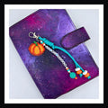 Oh My Gourd Charm features a handmade orange pumpkin charm with friendship-bracelet-style beaded tag that reads "oh my gourd" a teal paracord knot with bead details finishes this bag or planner charm.  