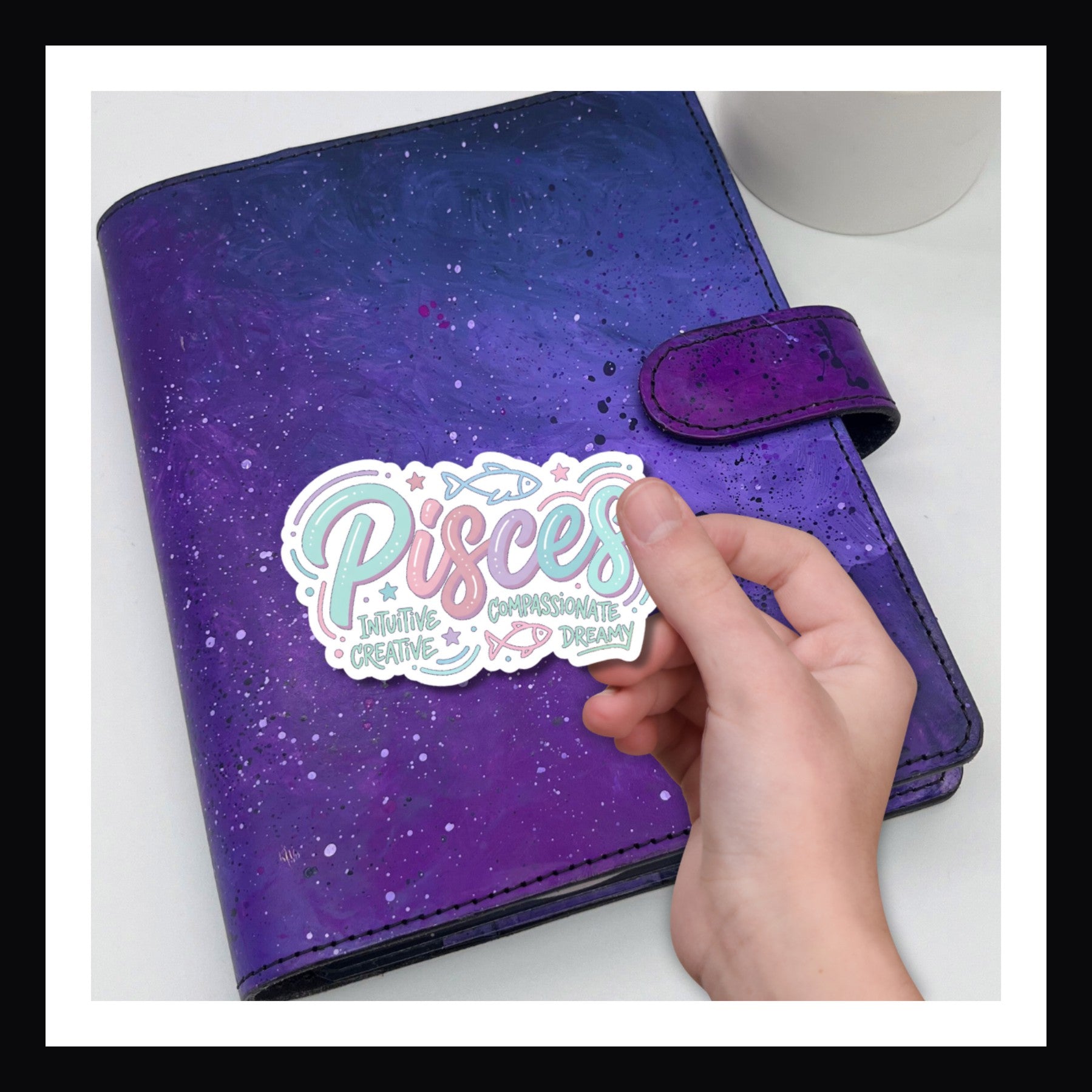 Purple planner with a 'Pisces' sticker held by a hand on a white background