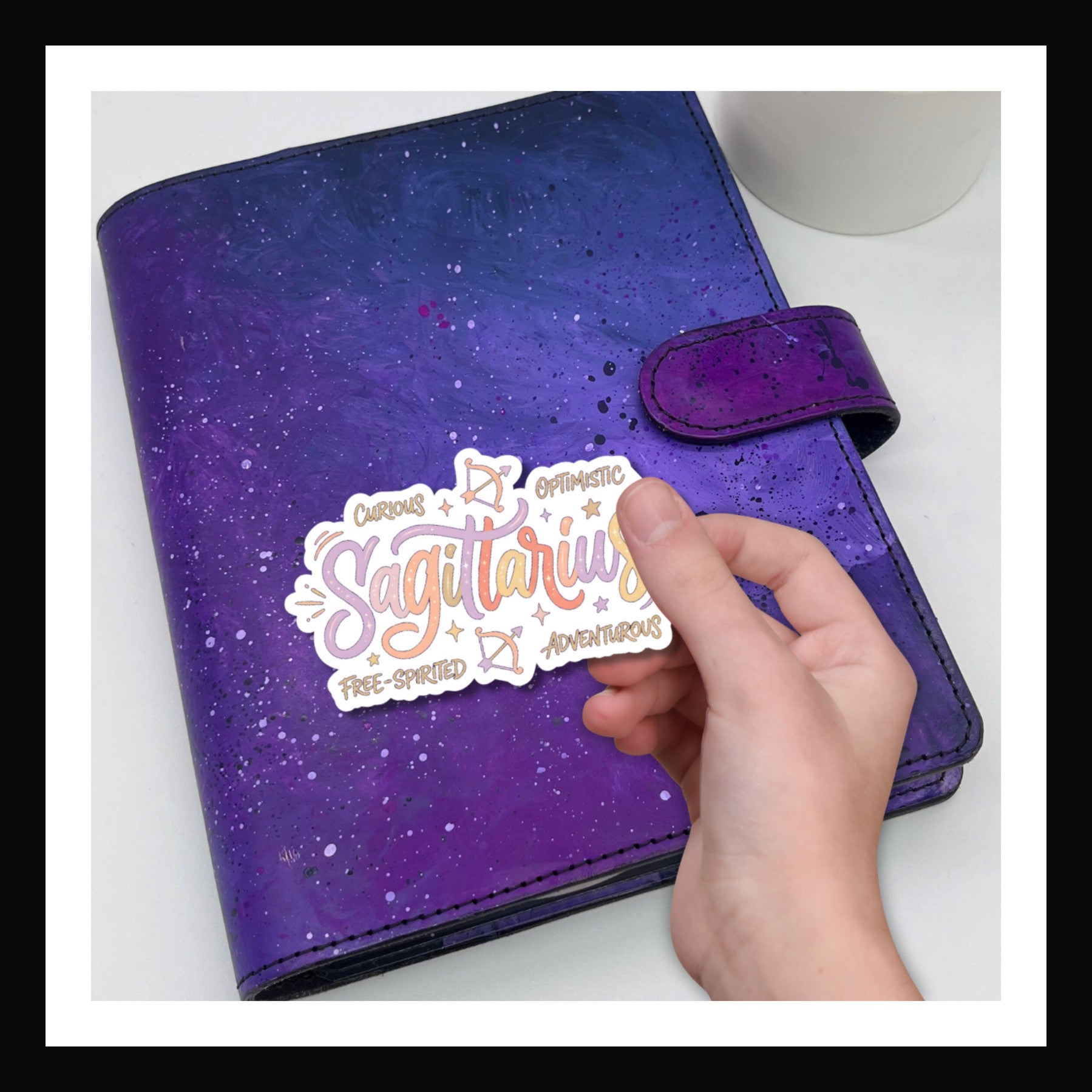 Purple planner with a 'Sagittarius' sticker held by a hand on a white background