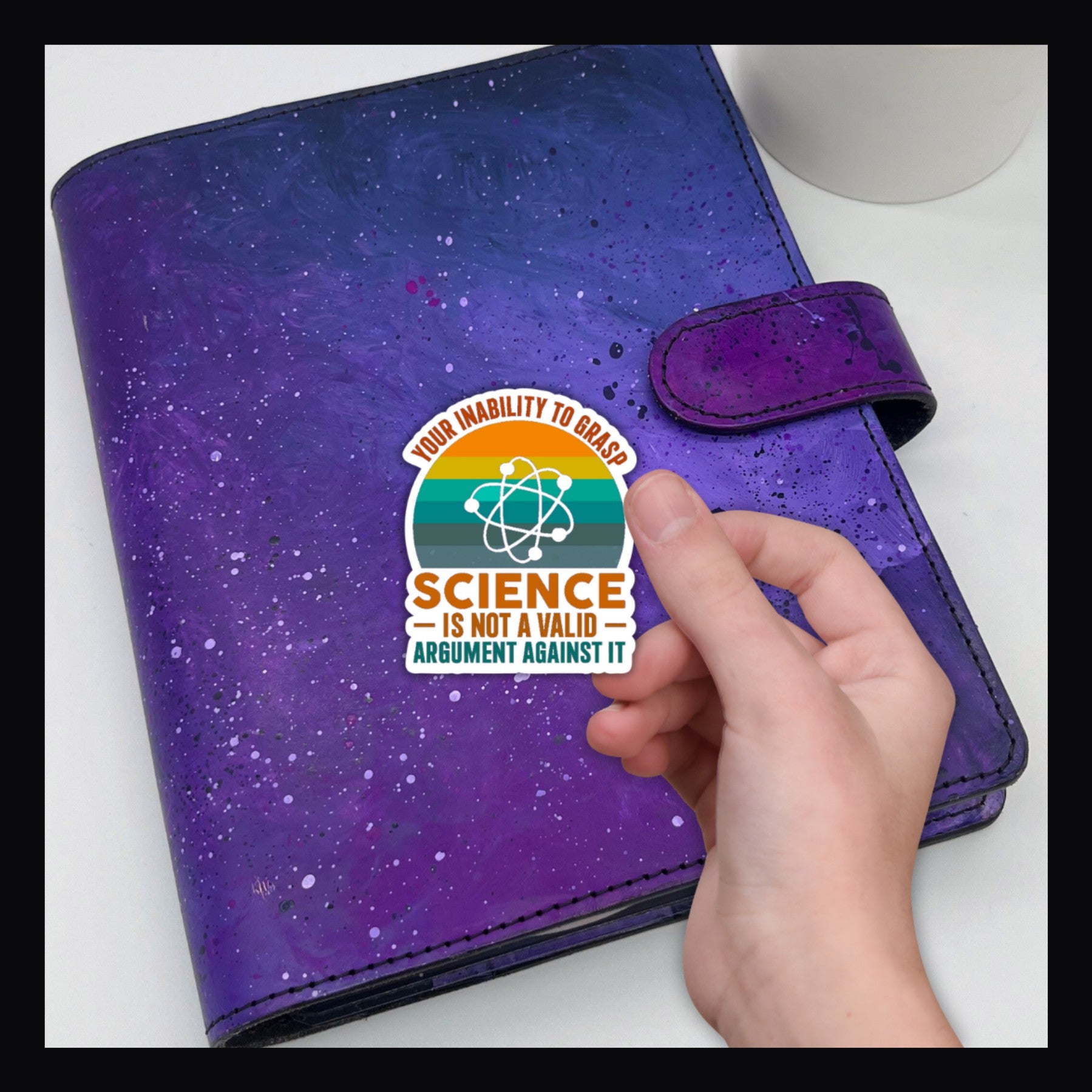 Science Die Cut Sticker reads "your inability to grasp science is not a valid argument against it". held over a purple planner.