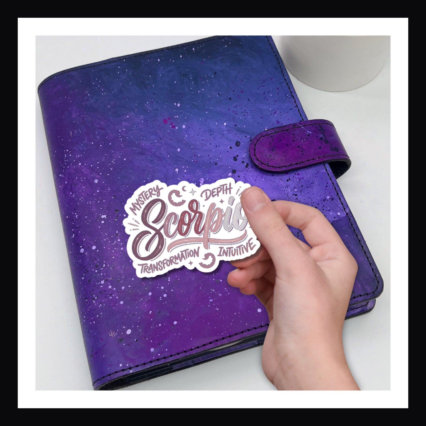 Purple planner with a Scorpio sticker held by a hand on a white background