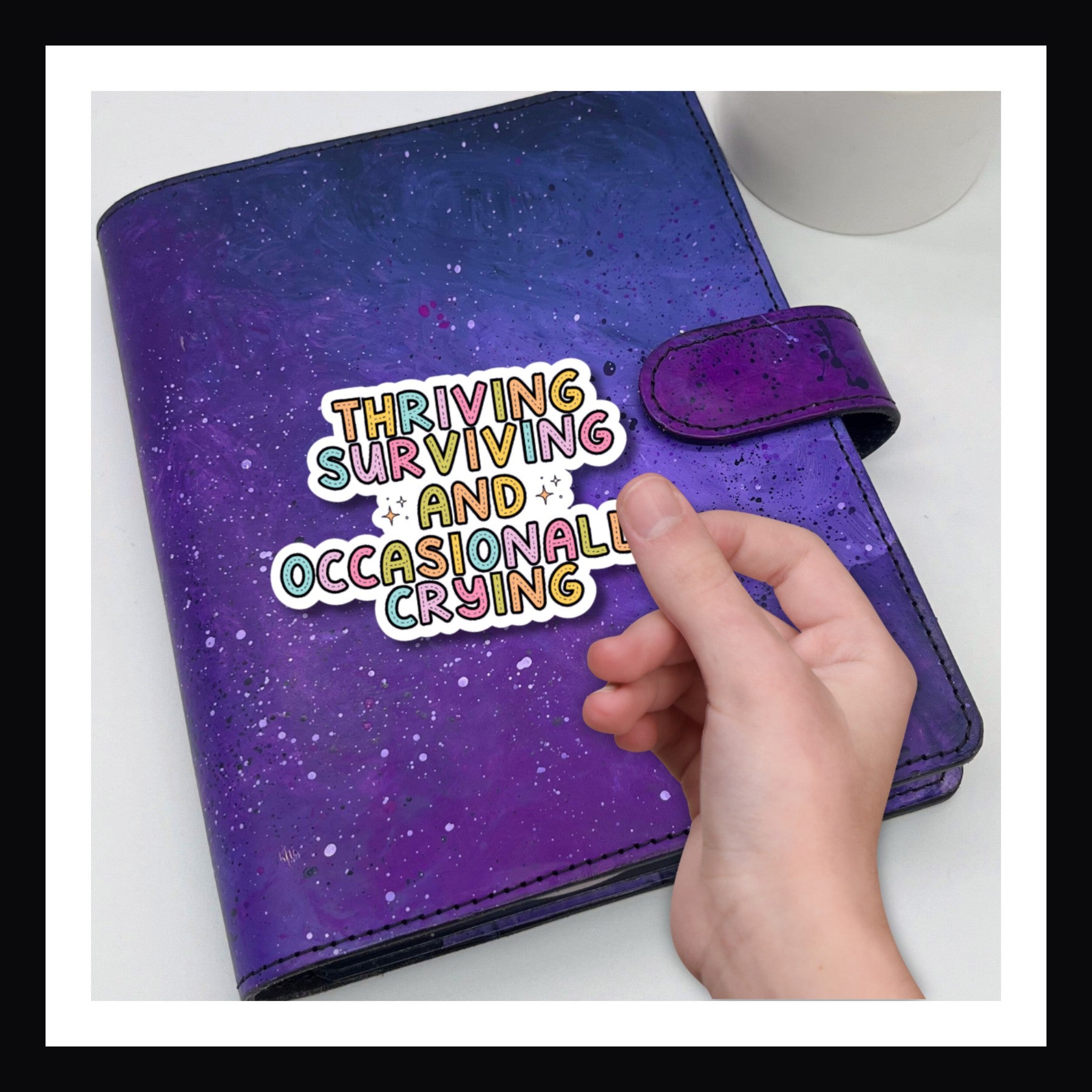 Thriving, Surviving, Crying Die Cut Sticker shown here on a purple planner.