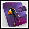 A candy corn charm with smiling face paired with black braided paracord and friendship bracelet style tag that spells out "Tricky".  Secure with a lobster clasp.