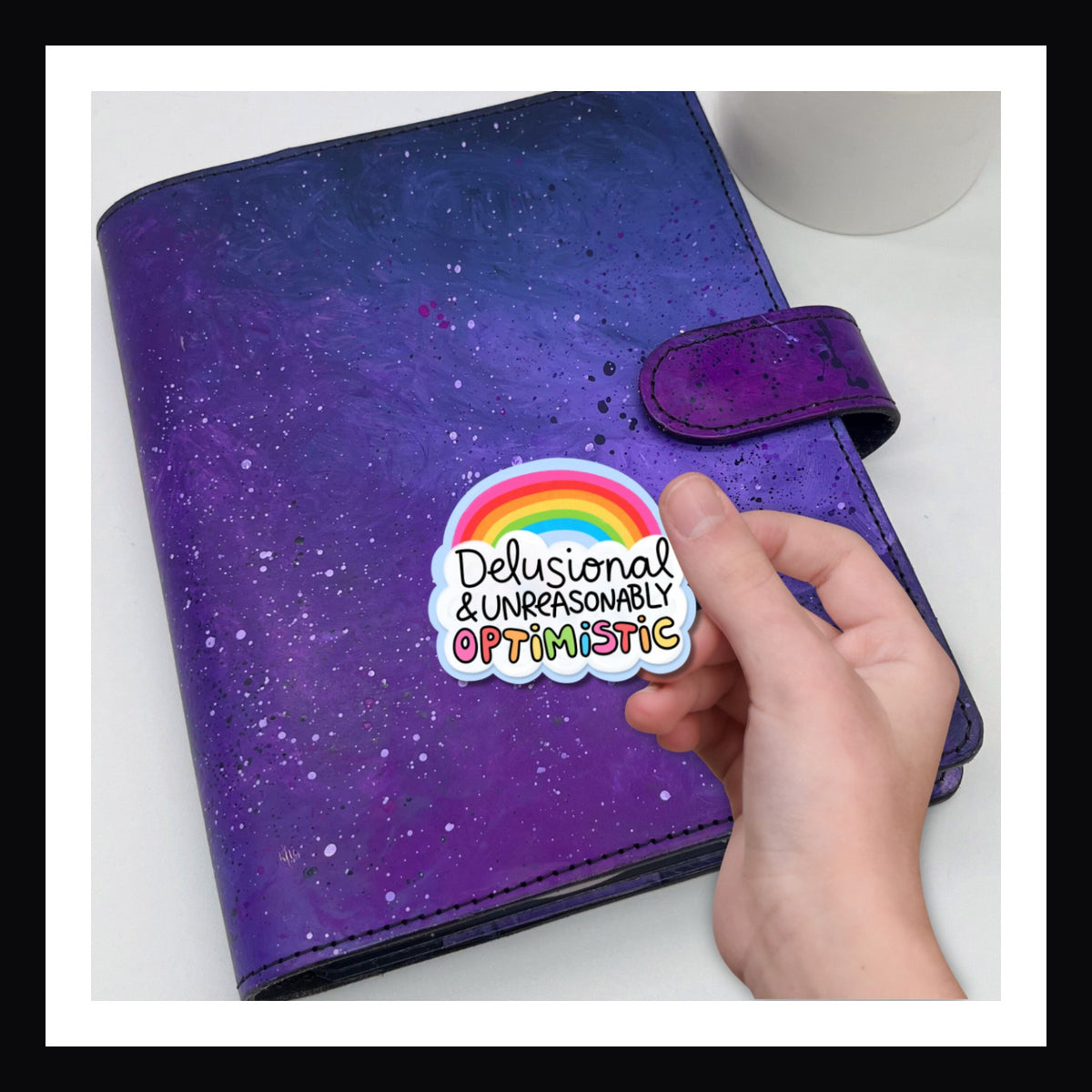 Unreasonably Optimistic die cut sticker features a bright rainbow and the statement "Delusional & Unreasonably Optimistic"