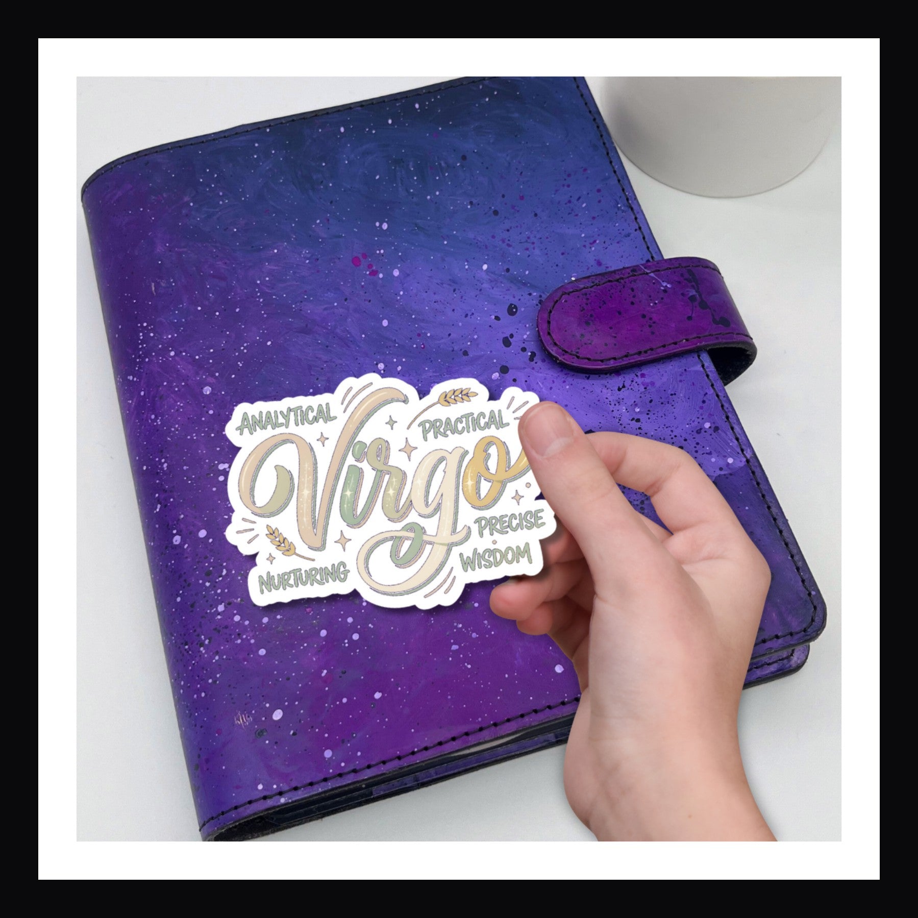 Purple planner with a  Virgo' sticker held by a hand on a white background