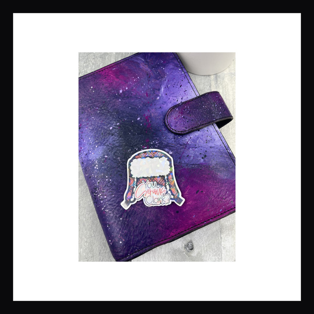 Holographic die cut sticker featuring a red flannel trapper hat and the quote "You Serious Clark?"